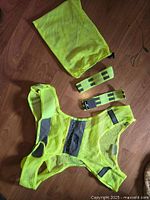 Full view of yellow mesh running safety vest, matching arm bands, and yellow drawstring storage bag laid out on wooden floor