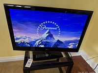 LG television turned on displaying Paramount HD splash screen, the television sits on black stand with remote control on stand.