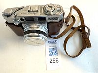 Top and front view of Aires 35-V camera in brown leather half case with lens cap and attached leather strap