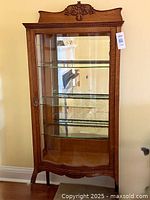 Full frontal view of the oak display cabinet showing bowed glass door, three shelves and carved details