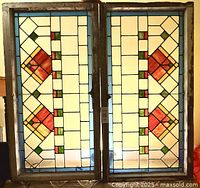 Front view of the pair of stained glass windows in original wooden frames showing geometric red/orange diamond motifs, clear textured panes, and blue border.