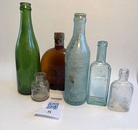 Photo of all 6 vintage glass bottles arranged side by side on a white background showing variations in color and size.
