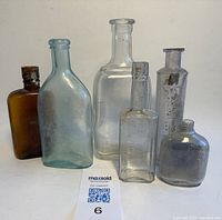 All six assorted vintage bottles grouped together showing various shapes, colors and sizes ranging from about 3 to 8 inches tall on a plain white surface.