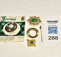 Lot of five brooches and stick pin arranged on flat surface with auction number card