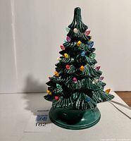 Full view of green textured ceramic Christmas tree with multi-colored candelabra bulbs attached and sitting on round green ceramic base.