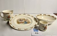 Photo showing full set of Bunnykins dishware pieces - plate, bowl, mug, and egg cup with Bunnykins illustrations and decorative border.