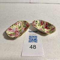 Pair of small rectangular floral chintz-patterned porcelain trays with scalloped edges and gold trim, shown on white background with lot number
