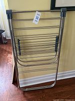 Folded metal drying rack standing against a wall showing the compact form and metal rod structure.