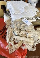 White folded fabric with intricate scroll pattern and bag of antique beige lace on spools and loose cuts on a red bag.