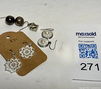 Four pairs of earrings displayed flat: a pair of beaded white pendant earrings on a brown cardboard, silver round drop earrings with mother of pearl inlay, and two pairs of silver earrings.