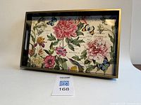 Full view of rectangular vanity tray showing floral pink peonies, green leaves, butterflies botanical design inside, black sides, and gold edge