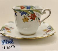 Teacup and saucer set showing detailed floral pattern and Tudor shape with scalloped edges and gold trim.