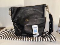 Front view of black leather bucket bag showing gold monogram initials AWT and part of the Henri Bendel dust bag underneath.