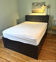 Full view of the assembled IKEA Brimnes double bed frame with white mattress cover in place, showing the tall headboard and surrounding room context.