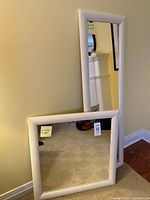 Two IKEA 'Riska' mirrors leaning against a yellow wall; one rectangular and one square, both with white painted wood frames.