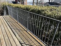 Long straight railing section on deck overlooking hedge and water view