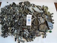 Top-down view of mixed grey LEGO pieces including platforms, vehicle shells, arches, and small parts spread out on a white surface.