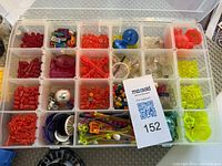 Compartmentalized plastic box with multiple slots containing various small Lego parts including neon clear pieces, flames, rods, round pieces, and small connectors sorted by color.