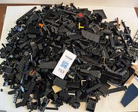 Pile of assorted black Lego pieces mixed with a few colored pieces on a flat surface with lot tag.