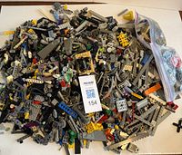 Loose pile of mixed LEGO pieces including grey Technic and colorful specialty bricks spread on a flat white surface with a Masold label for lot 154