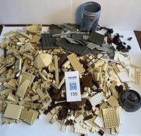 Loose assorted Lego pieces in white, brown, and tan colors piled with a Lego storage tin visible, showing variety of parts including platforms, arches, smaller pieces from multiple Lego themes.