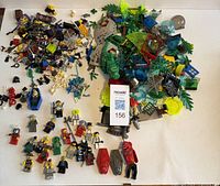 Overview of the entire collection showing mini figures, plant pieces, animal figurines, accessories, and skeleton parts spread out on a white surface with a lot tag.