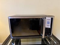 Closed microwave showing stainless steel finish, black windowed door, and right side control panel with keypad and handle.