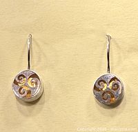 Front view of the pair of round silver earrings featuring a gold three wave swirl design on the face and French wire hooks.