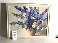 Front view of needlepoint art depicting vase with blue delphiniums and daisies in metal frame