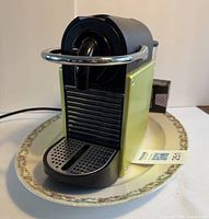 Front view of Nespresso Type D60 coffee maker on oval Limoges platter showing black and yellow sides with drip tray and power cord