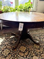 Front view of round oak dining table top with natural light from window, showing surface wear and wood grain.
