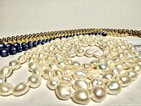 All four necklaces arranged close together showing different beads: white freshwater pearls, blue beads, faux pearls, and gold-colored metal beads.