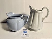 Two pitchers side by side showing blue 'Greydawn' milk pitcher and white ironstone pitcher.