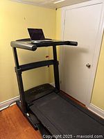 Treadmill unfolded in desktop configuration against yellow wall with laptop