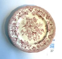 Photo showing cream base plate with cranberry red floral transfer pattern from above, scalloped edges visible.