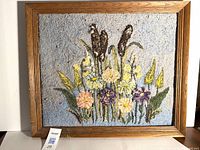 Front view of rug-hooked artwork framed in oak, showing floral wildflower and bullrush in textured yarns on blue background.
