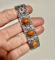 Close-up showing the filigree silver bracelet with three oval cabochon orange stones, detailed floral design in silver