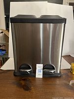 Front view of the stainless steel dual compartment trash can with two step pedals at the base.