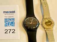 Two Swatch watches side by side on a cloth background, showing the men's black watch and women's gold-coloured watch.