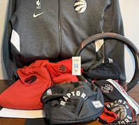 Full lot displaying red and grey hoodies, black Herschel fanny pack, steering wheel cover, red shirts, masks and black T-shirt all arranged for appraisal.