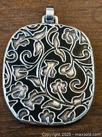 Close-up of the front of the Tous silver pendant with black enamel floral pattern and silver scroll design.
