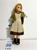 Front view of Anne of Green Gables doll showing red braided hair, brown dress, white apron, green straw bonnet and black felt boots with open toes.