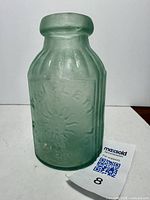 Front view of the blue-green ribbed bottle with embossed sun motif and 'W&J Flett Liverpool' text.