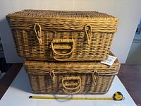 Two stacked wicker hamper-style baskets, showing external front, closures, and handles, with tape measure for size reference.
