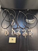 Five black cord necklaces with abalone and silver pendants arranged on a dark wooden surface, showing the overall lot content