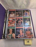 Top-down view of first binder page showing nine NBA Hoops basketball cards including Charles Smith, James Worthy, Jerome Richardson, Akeem Olajuwon, Dennis Rodman, Xavier McDaniel, Larry Bird, Tom Chambers, and Scottie Pippen.