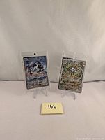 Two Pokémon cards displayed on clear stands, one Chien-Pao EX 261 SIR in protective sleeve and one sealed Magneton Promo 159 wrapped in plastic.