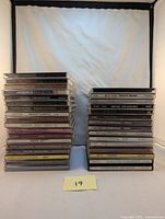 Two stacked towers of classic rock CDs with visible titles and artists such as Journey, Led Zeppelin, Genesis, INXS, Styx, Motley Crue, Dr. Hook and Supertramp.