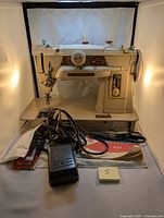 Full view of Singer 401 G sewing machine on platform with foot pedal and manual in front under warm lighting.