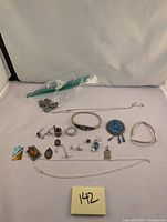 Photo showing the laid out silver jewelry including bracelets, pendants, earrings, necklaces, and small parts with a plastic bag containing smaller pieces.